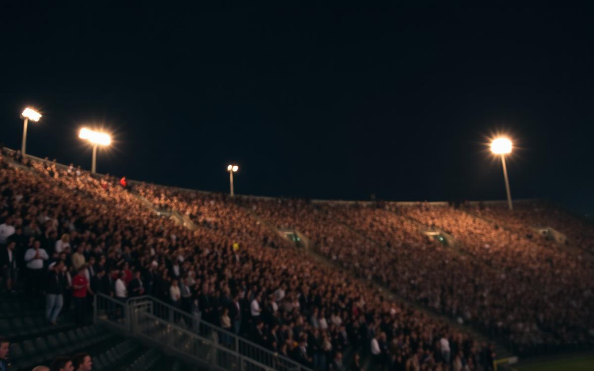 Packed American football stadium under floodlights before a night kickoff